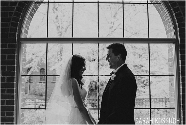Black and white, bride and groom embrace in front of window